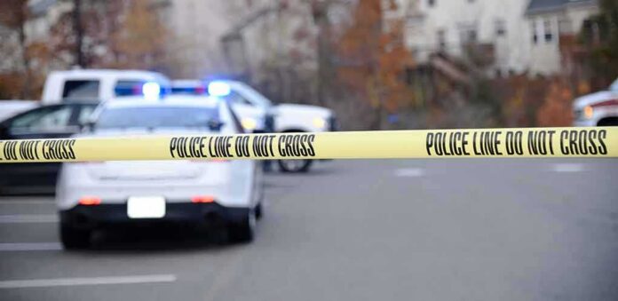shutterstock_1230120343 Police tape cordons off a street with patrol cars and flashing lights in the background