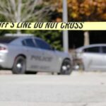 Sheriff's line tape blocking a street with police cars behind