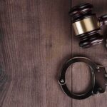 Judge’s gavel and metal handcuffs on wooden table