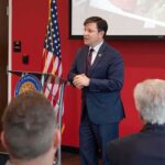 House Republican Fights Abuse Accusations Speaker in a navy suit addressing an audience at a podium