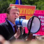 Governor Signs Controversial Abortion Measure Man speaking into a megaphone at a rally