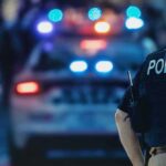 police officer in vest near patrol car with flashing lights