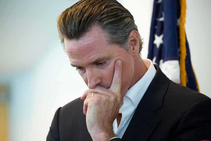 shutterstock_1747778459 Gavin Newsom in a pensive pose with hand on face near a U.S. flag