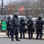 Panic Erupts: Armed Man Charges Candidate Group of police officers in riot gear standing on a street; Brian Folkerts present