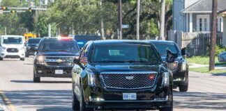 Motorcade of black SUVs and sedans driving down a city street
