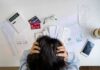 America’s Economic Numbers Tell Two Stories Person holding head over bills and credit cards on desk