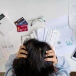 Person holding head over bills and credit cards on desk