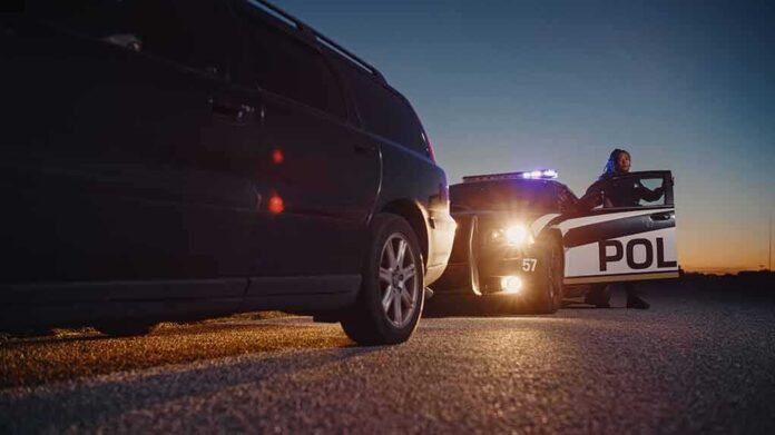 shutterstock_2232055739 Police officer at patrol car during traffic stop at dusk