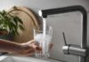 EPA Hunt: What’s Hiding In Faucets? Hand holding a glass under a kitchen faucet