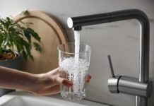 EPA Hunt: What’s Hiding In Faucets? Hand holding a glass under a kitchen faucet