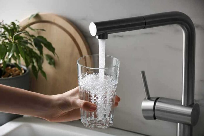 shutterstock_2247078069 Hand holding a glass under a kitchen faucet