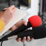 Early-State Moves Hint At Bigger Play Journalist holding two microphones while writing in a notebook