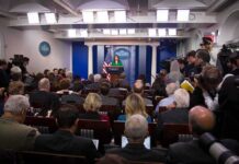 White House Purge Ignites Press War Press secretary at podium addressing reporters in briefing room