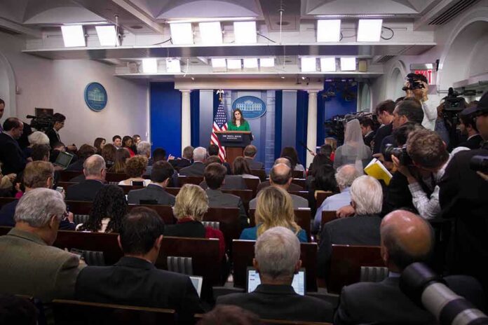 shutterstock_744405130 Press secretary at podium addressing reporters in briefing room