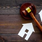 Judge's gavel with paper house cutouts on wooden table