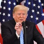 Donald Trump speaking at a podium with American flags in the background