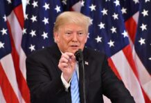 Shock Nobel Pick Sparks Trump Fury Donald Trump speaking at a podium with American flags in the background