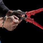 Hands in handcuffs being cut with red bolt cutters