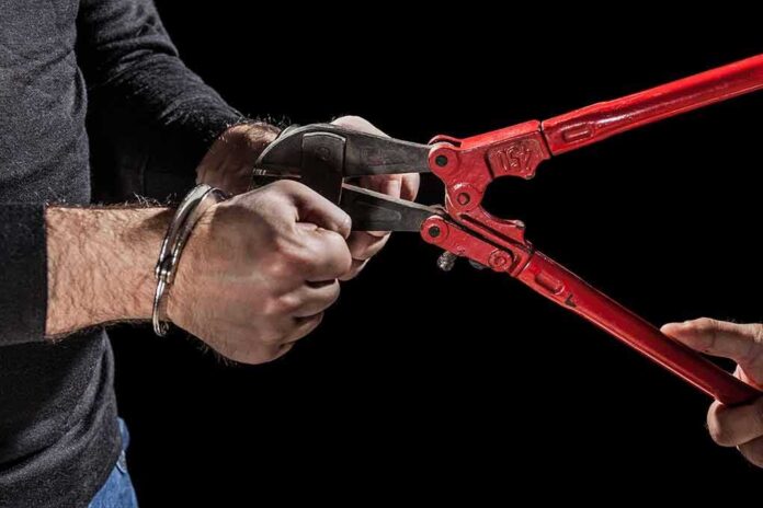 Hands in handcuffs being cut with red bolt cutters