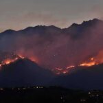 Wildfire burning along mountain slopes at dusk