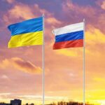 Ukrainian and Russian flags on poles at sunset