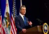 Gavin Newsom speaking at a podium with U.S. and California flags