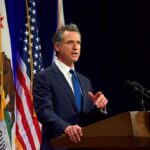 Gavin Newsom speaking at a podium with U.S. and California flags