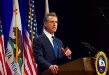 Gavin Newsom speaking at a podium with U.S. and California flags