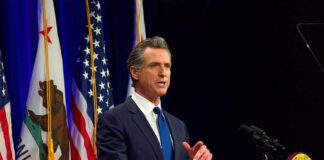 Gavin Newsom speaking at a podium with U.S. and California flags