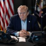 Shock Move: Trump Eyes Ambassador Ouster Donald Trump seated at a table between two desk phones