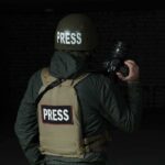 Press photographer in helmet and vest holding a camera