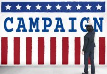 Political Ad Text Blast Called Antisemitic Man in suit writing on large campaign banner with stars and stripes